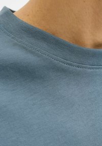 Svetlomodra bombažna majica z gladko teksturo, okroglim izrezom in preprostim šivom na ovratniku.