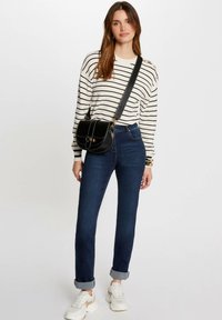 Schwarze Umhängetasche mit goldenen Beschlägen, weißer Pullover mit schwarzen Streifen, blaue Jeans und weiße Sneaker mit beigen Akzenten.