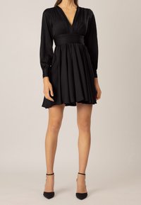 Svart klänning med djup V-ringning, långa ärmar och en figurnära överdel med en utsvängd kjol. Mjuk textur med subtila veck.