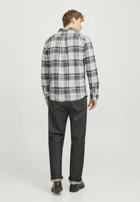 Heren geruite shirt in zwart en grijs, met een button-down kraag, gecombineerd met donkere spijkerbroeken, met opgerolde mouwen en zwarte boots.