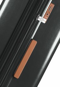 Valigia rigida nera con doppia zip, lucchetto a combinazione e un manico in vetro marrone testurizzato. Superficie liscia e lucida con hardware distintivo.