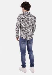 Camicia a righe bianche e nere con colletto, abbinata a jeans blu e sneakers bianche. Il tessuto presenta un motivo floreale.