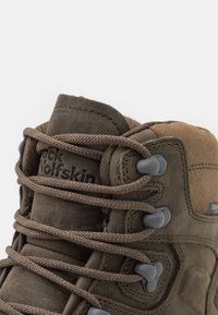 Brun vandringsko med övre del av läder och mocka, texturerad yta, grå snörning och metallöglor. Har "Jack Wolfskin"-logotypen på sidan.