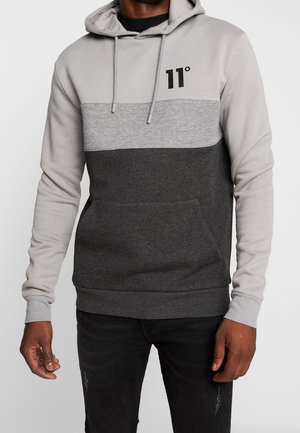 Mann trägt Color-Block-Hoodie mit hellgrauer Kapuze und Ärmeln, mittelgrauer Brust, dunkelgrauem Oberkörper und "11°" Logo auf der Brust.
