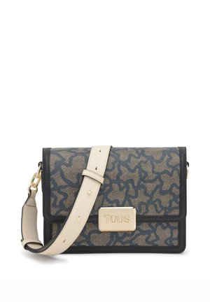 Bolso bandolera estampado en topo y azul marino, con ribete negro, correa ajustable de color crema, herrajes dorados y cierre frontal con el logotipo de Tous.