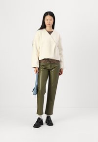 Kremfarget fleece-inspirert jakke over en leopardmønstret topp, sammen med olivengrønne imitationlærbukser og svarte loafers. Blå håndveske som aksent.