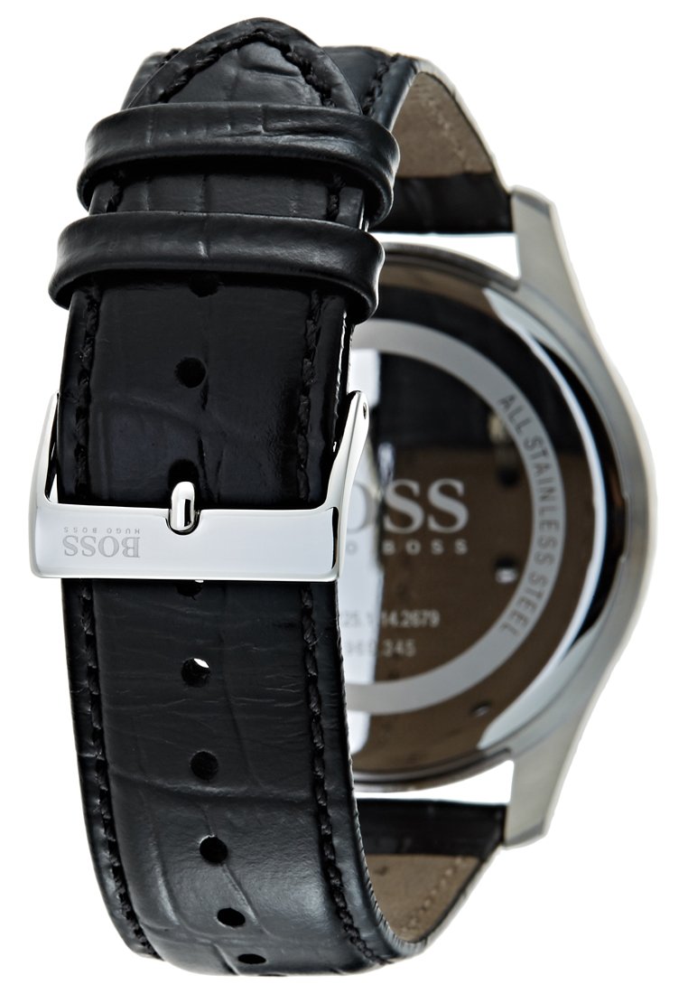 Bracelet de montre en cuir noir avec texture crocodile, boucle en métal argenté, et un boîtier en acier inoxydable visible en arrière-plan.
