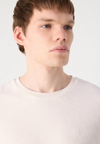Kortärmad krämfärgad T-shirt i texturerad bomull, med rund hals och diskret logodetalj på bröstet.