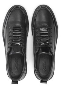 Zapatillas de cuero negro con una textura lisa, que presentan cordones elásticos, un acento brillante sobre la lengüeta y una resistente suela de goma.