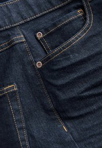 Donkerdenim jeans met een soepele textuur, voorzien van contrasterende oranje stiksels en metalen accenten op zakken en sluitingen.
