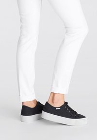 Juodos drobės kedai su balta guma, apvaliu nosiu ir šnuromis, derinami su suveržtomis baltomis kelnėmis.