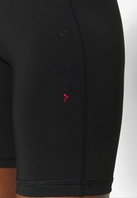 Sorte atletiske shorts lavet af strækbart stof. Har branding i glat sort på siden og røde accenter tæt på kanten.