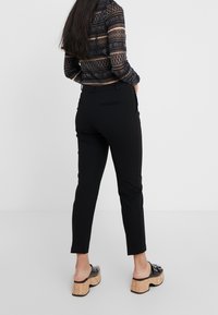 Svarta avsmalnande byxor med bältesloopar och bakfickor. Bärs med en genomskinlig mönstrad topp och svarta plattformssandaler med korksulor.