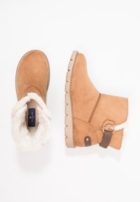 Bottines en daim beige avec une doublure blanche duveteuse, un détail à sangle marron et une semelle en caoutchouc texturée avec des rainures.