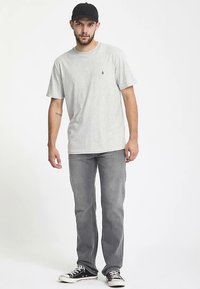Graues Baumwoll-T-Shirt mit kurzen Ärmeln, kombiniert mit ausgewaschenen grauen Jeans. Schwarze Baseballkappe und schwarze Sneakers mit weißen Sohlen vervollständigen das Outfit.