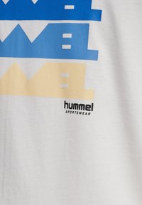 Vit bomullströja med blå och gula grafiska texter, med "hummel"-logotyp i svart. Texten har geometriska former och varierande höjder.