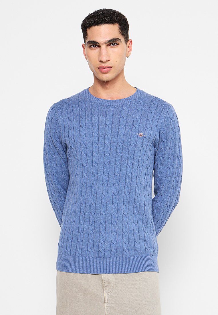 Suéter de punto azul claro con diseño de trenzas, cuello redondo y puños y dobladillo de canalé. Pequeño logo cerca del pecho. Tela de algodón.