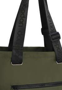 Bolsa de tela verde con correas ajustables de textura negra. Presenta un prominente bolsillo con cremallera en la parte frontal y acentos de metal.