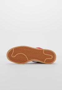 Röd sula på sneakers med ett texturerat gummitread som har ett fiskbensmönster. Förstärkt tåområde och kontrasterande vita sidokanter.