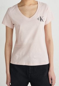 Světle růžové bavlněné tričko s výstřihem do V a krátkými rukávy. Na levém prsu se nachází černé logo Calvin Klein Jeans. Klasický střih.