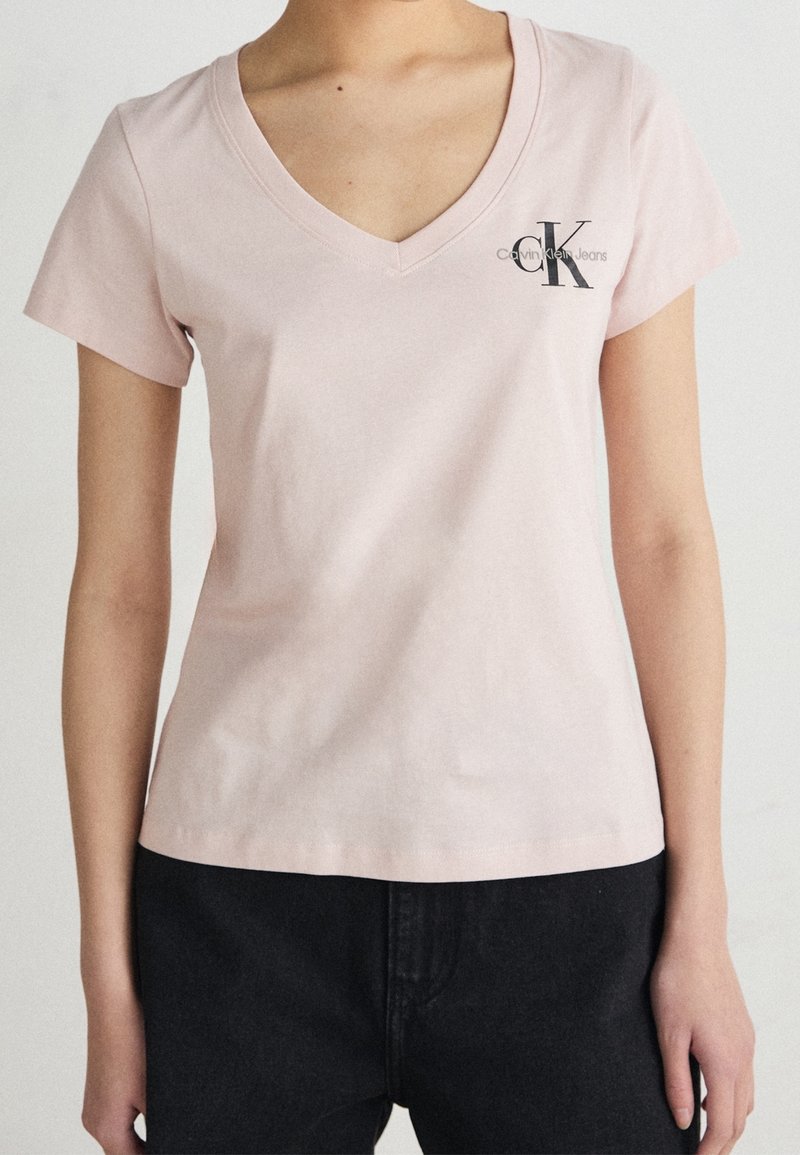 Světle růžové bavlněné tričko s výstřihem do V a krátkými rukávy. Na levém prsu se nachází černé logo Calvin Klein Jeans. Klasický střih.