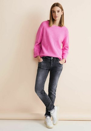 Suéter de punto rosa con patrón texturizado, de corte relajado, combinado con jeans gris oscuro y zapatillas blancas. Ambientado en un fondo neutral.