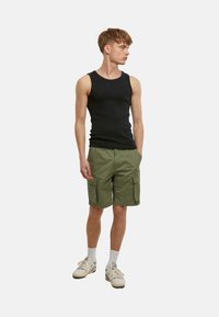 Débardeur noir sans manches et short cargo vert olive avec plusieurs poches, porté avec des chaussettes blanches et des baskets beiges.