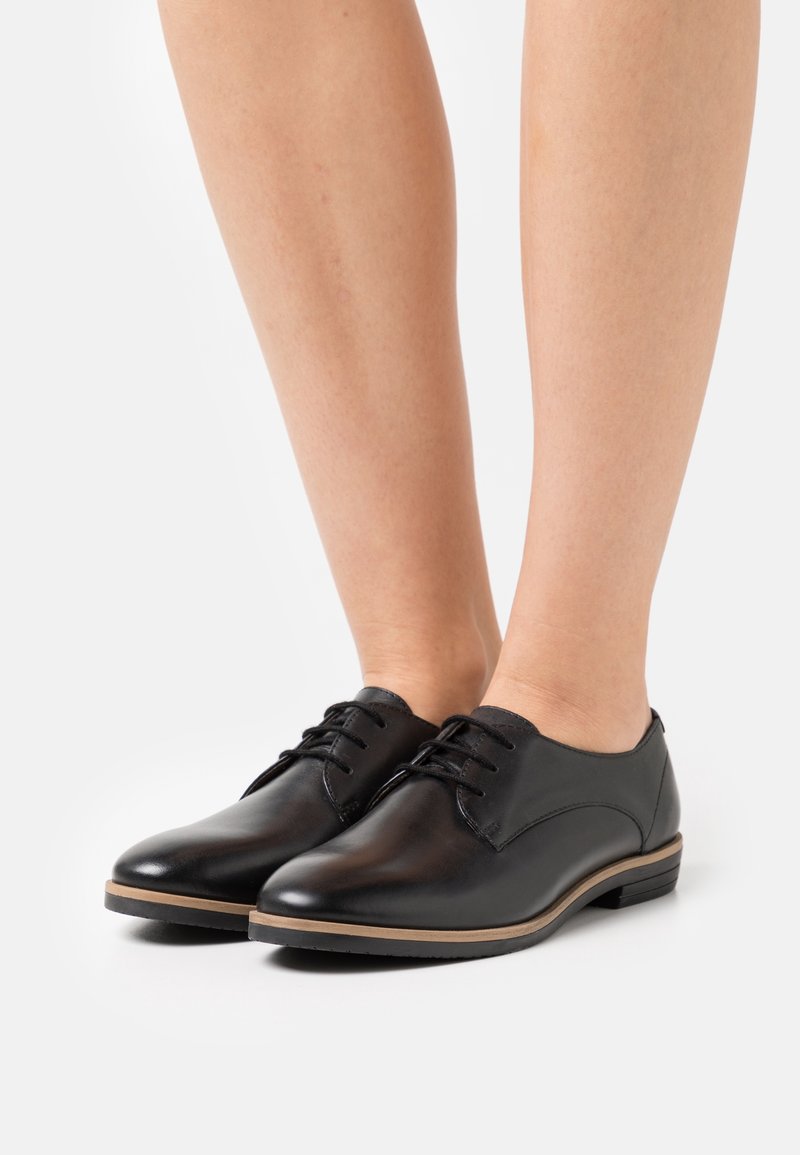Chaussures en cuir noir à finition lisse, bout arrondi et petit talon empilé, avec un design à lacets et des accents marron subtils le long de la semelle.