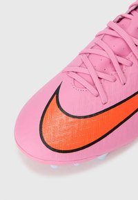 Pink atletiske sko med en tekstureret overflade, der har et fremtrædende orange Nike-logo med sort omrids. Snørebåndene er synlige i toppen.
