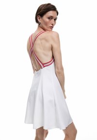 Weißes Kleid mit einem ausgestellten Design, ausgestattet mit rot-weißen gestreiften Kreuzträgern und einem glatten, leichten Stoff.