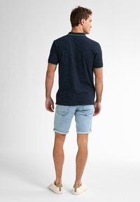 Polo navy con rayas horizontales texturizadas, con acentos en el cuello de color verde, combinado con pantalones cortos de mezclilla azul claro y zapatillas beige.