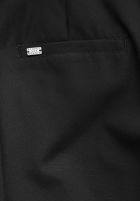 Schwarzer Stoff mit einer glatten Textur, ausgestattet mit einer rechteckigen Tasche und einem kleinen, silbernen Etikett mit der Aufschrift "STREET ONE STUDIO."