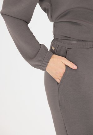 Graues Langarmshirt mit entspanntem Schnitt und elastischen Bündchen. Die engen Hosen verfügen über eine Seitentasche und einen subtilen Glanz, hergestellt aus weichem Material.