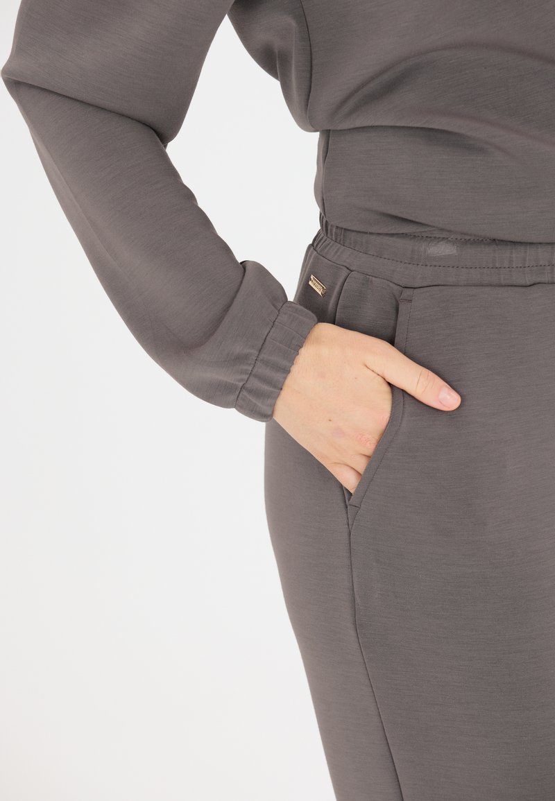 Graues Langarmshirt mit entspanntem Schnitt und elastischen Bündchen. Die engen Hosen verfügen über eine Seitentasche und einen subtilen Glanz, hergestellt aus weichem Material.
