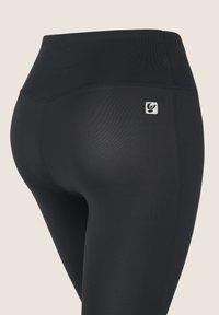 Leggings sportivi neri a vita alta visti dal lato destro posteriore, con un piccolo logo bianco vicino alla vita.