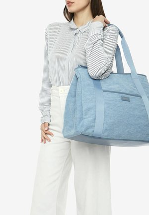 Borsa a tracolla blu in tela con tessuto testurizzato e spallacci lisci, dotata di una tasca frontale e un design strutturato, tenuta da una persona in una maglietta a righe.