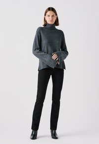 Donkergrijze coltrui met geribbelde manchetten en een ontspannen pasvorm, gecombineerd met zwarte slim-fit broeken en enkellaarzen. Eenvoudig en modern ontwerp.