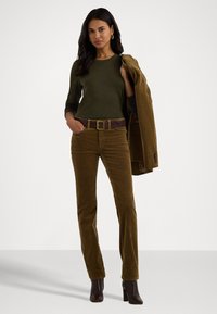 Brune corduroy bukser med lige pasform, parret med en mørkegrøn langærmet top og et brunt bælte, accessoriseret med en brun jakke.