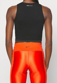 Czarny, krótki top sportowy z teksturowanym pasem w talii, w zestawie z pomarańczowymi, błyszczącymi legginsami z logo Nike.