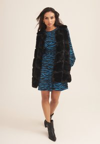 Black faux fur vest over a blue dress with black zebra stripes, featuring a fitted waist and short sleeves, paired with black ankle boots.