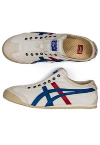 Scarpa di tela bianca con strisce blu e rosse, punta rotonda, sei occhielli neri e suola in gomma beige. Presenta un colletto imbottito e una soletta testurizzata.