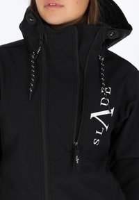 Czarna wodoodporna kurtka z wysokim kołnierzem, białym logo, zamkiem błyskawicznym z przodu oraz regulowanymi sznurkami, z czarnymi i białymi akcentami.