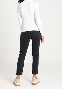 Top blanco de manga larga con costillas combinado con pantalones negros con dobladillo vuelto y zapatos plataforma beige, presentando un acabado texturizado en el top y pantalones de tela lisa.