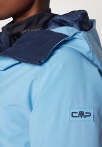 Giacca azzurra chiara con colletto navy, dotata di chiusura a zip e patch con logo CMP. Tessuto dalla texture liscia, progettata per l'uso all'aperto.