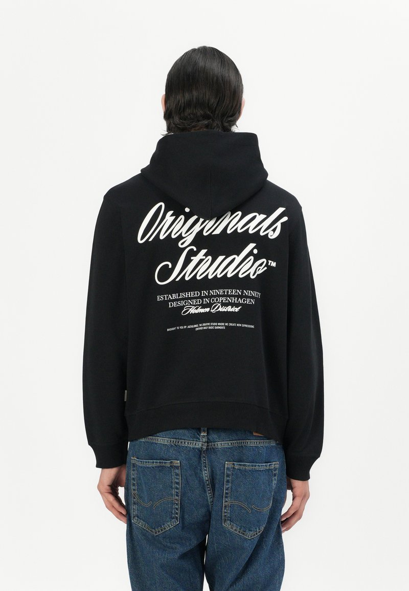 Black hooded sweatshirt with a cropped design. White text on the back includes "Originals Studio," established details, and a tagline.