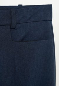 Gros plan sur un pantalon bleu foncé taillé, montrant la ceinture, la passants pour ceinture et la poche avant avec un tissu texturé.