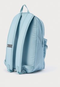 Ανοιχτό μπλε νάιλον σακίδιο με επενδυμένους ιμάντες, πλαϊνή τσέπη με φερμουάρ και μικρή ετικέτα με λογότυπο στο μπροστινό μέρος. Λείο υλικό, κυρτό σχήμα.
