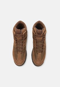 Stivali da trekking marroni con design in camoscio e mesh. Presentano una caviglia alta, collo imbottito, chiusura con lacci e suola in gomma antiscivolo.