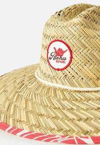 Cappello di paglia a tesa larga con una trama intrecciata, banda decorata in rosso e una patch rotonda con "Aloha Ripcurl" in nero e rosso.