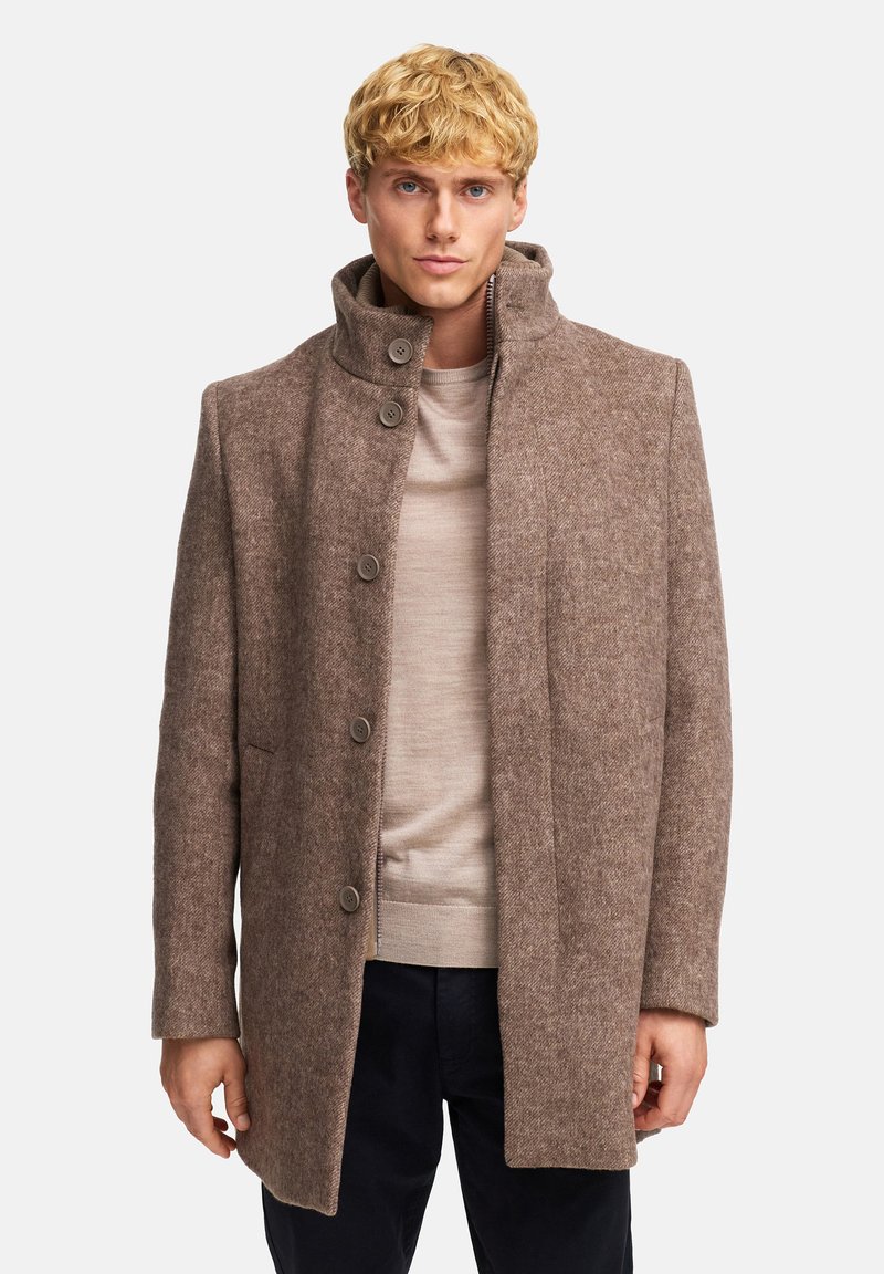 Abrigo de mezcla de lana marrón con cuello alto, tejido texturizado, cierres de botones y bolsillos laterales, llevado sobre un suéter beige.
